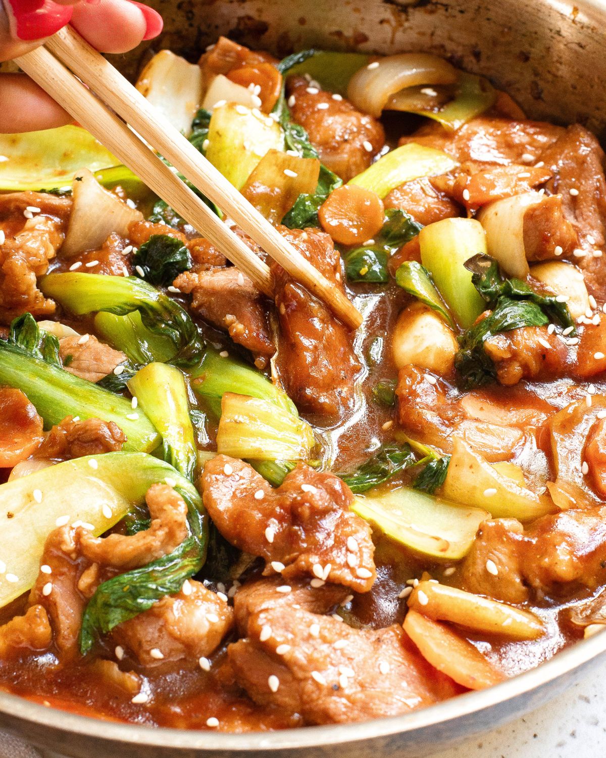 Homemade pork chop suey in a pan with chopsticks picking up some of the pork.