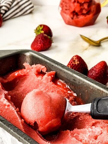 Strawberry sorbet in a loaf pan being scooped out of the pan.