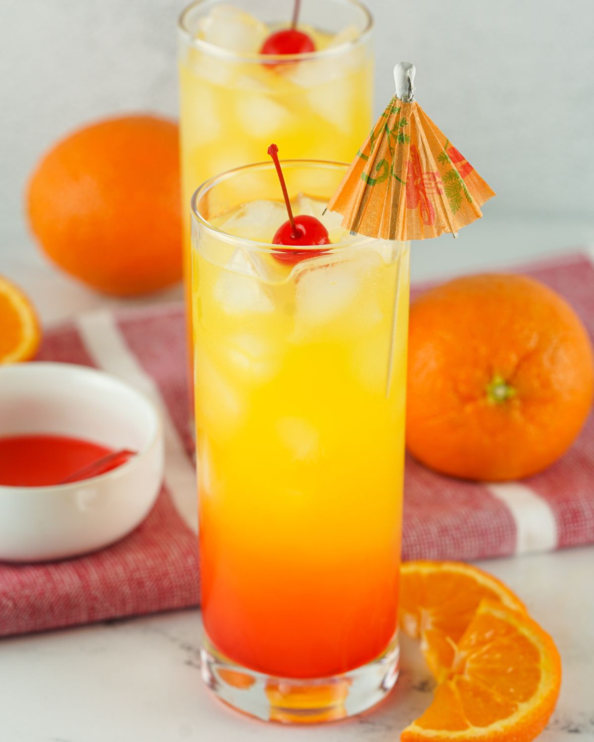 Tequila Sunrise Cocktail with a maraschino cherry and an umbrella in the cocktail.