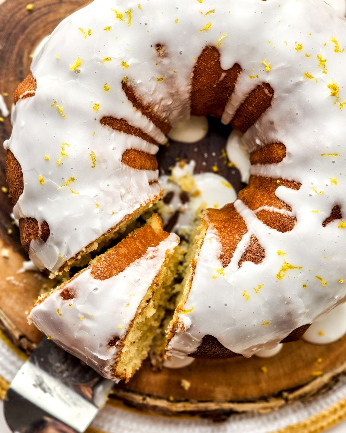 A lemon glazed bundt cake with lemon zest being sliced for serving.