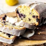 Blueberry lemon loaf with a glaze and sliced into pieces on a wooden blockj.