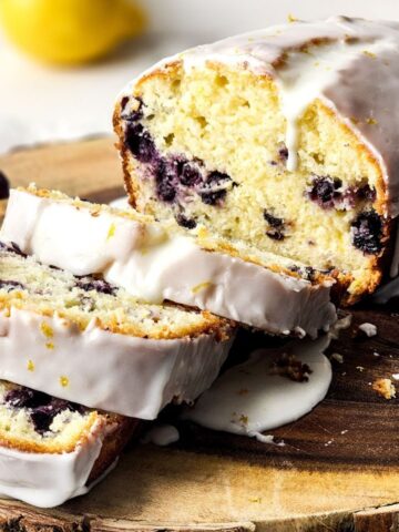 Blueberry lemon loaf with a glaze and sliced into pieces on a wooden blockj.