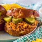A shredded hot honey chicken sandwich with pickles on a pretzel bun.