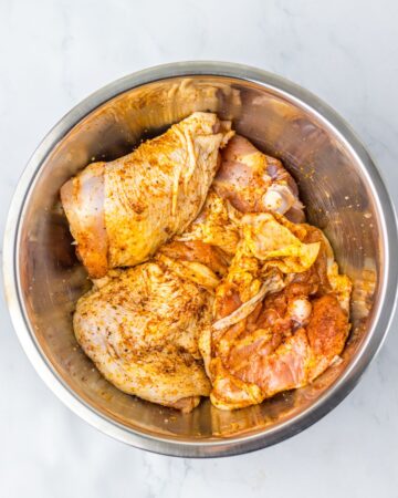 Chicken thighs rubbed with spices in a bowl to make apple cider chicken thighs. 