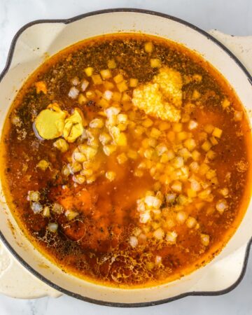 A large saute pan with apple cider, spices to make a sauce for apple cider sauteed chicken thighs. 