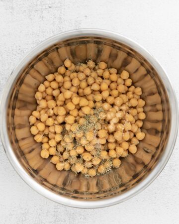 A silver bowl with chickpeas, rosemary, and garlic.