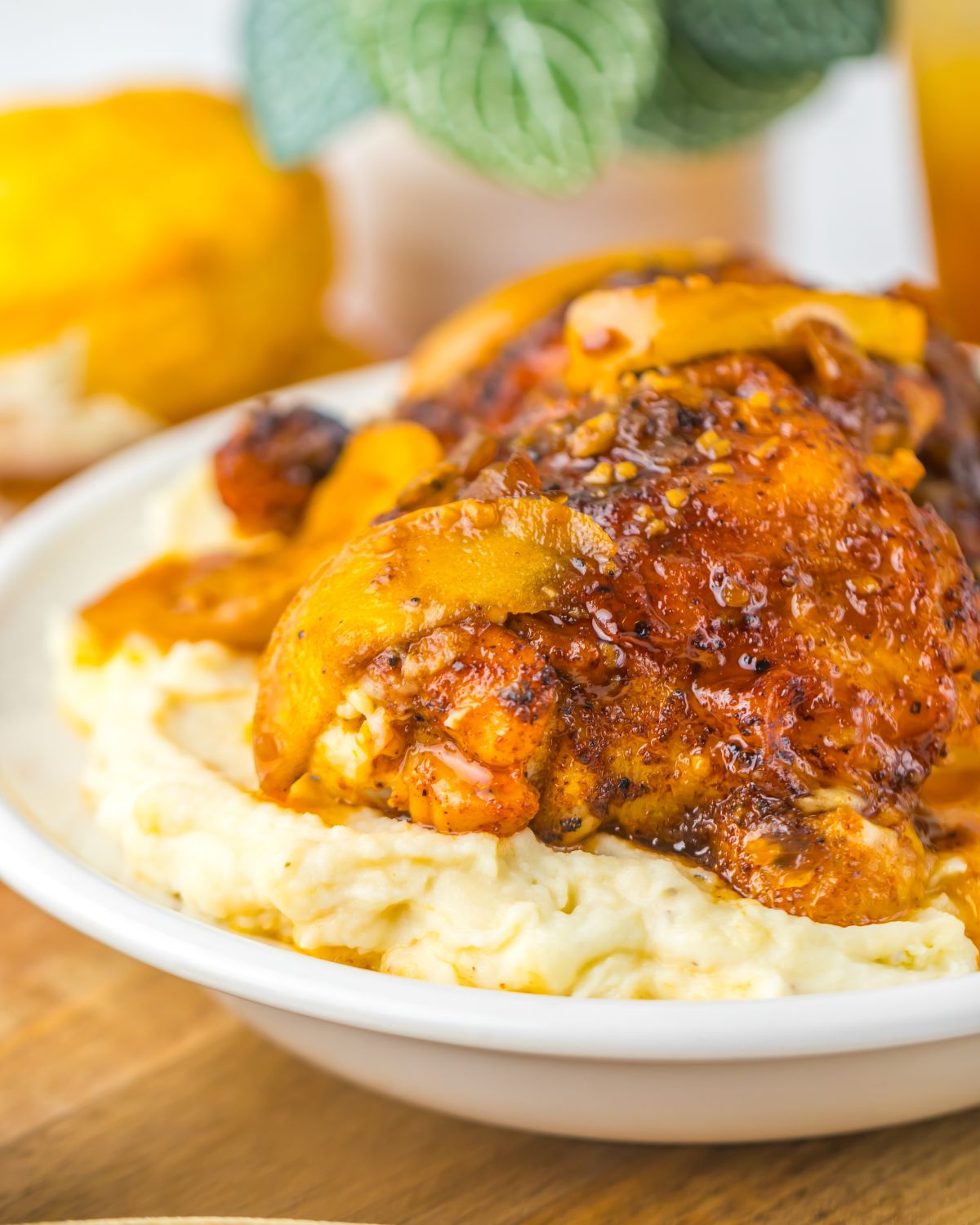 A large plate with mashed potatoes topped with chicken thighs in an apple cider sauce. 