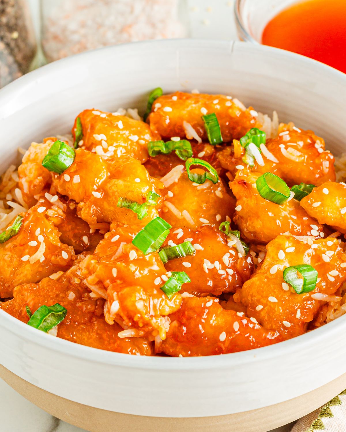 Chicken tender pieces with orange chicken sauce topped with sesame seeds and green onions. 