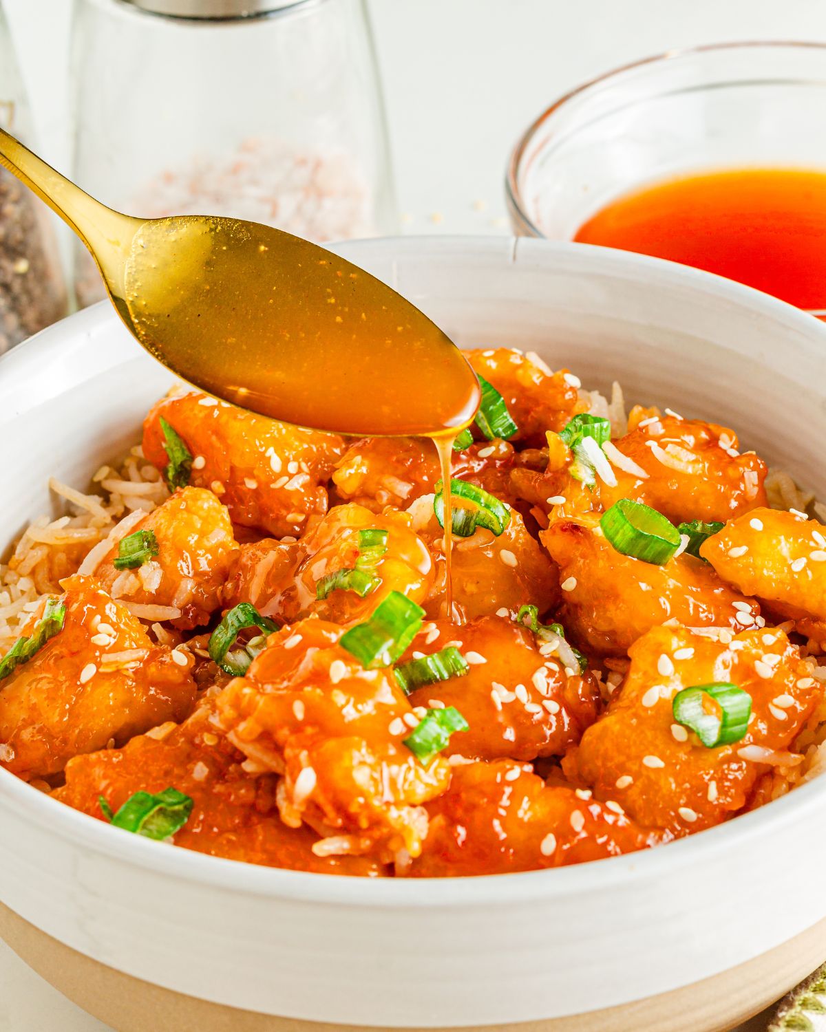 A large white bowl with orange chicken pieces topped with sesame seeds and chopped green onions. 