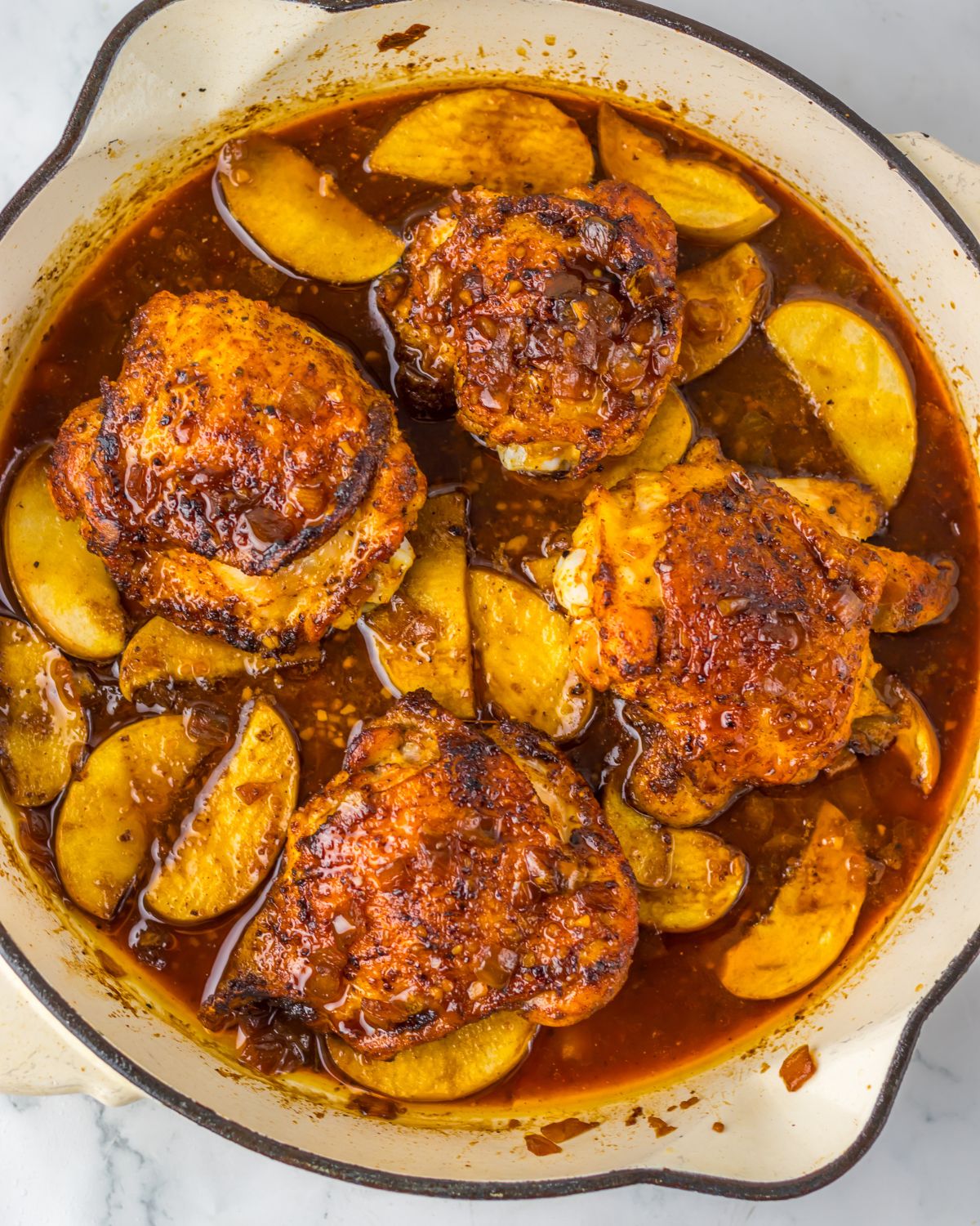 A large saute pan with seated chicken thighs and apples in an apple cider sauce. 