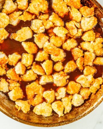 A saute pan with sauteed chicken pieces in an orange sauce. 