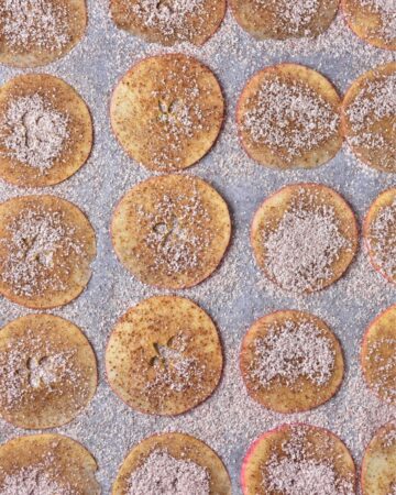 Apple slices on a baking sheet with a cinnamon sugar mix to make baked apple slices.