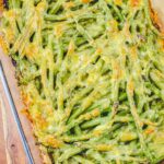Green beans topped with a cheesy sauce in a glass casserole.