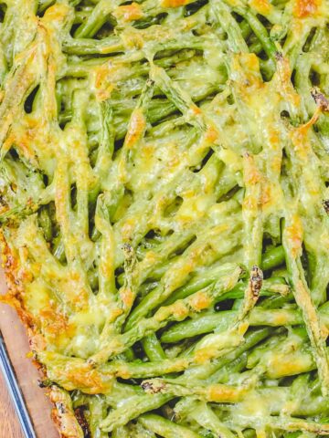 Green beans topped with a cheesy sauce in a glass casserole.