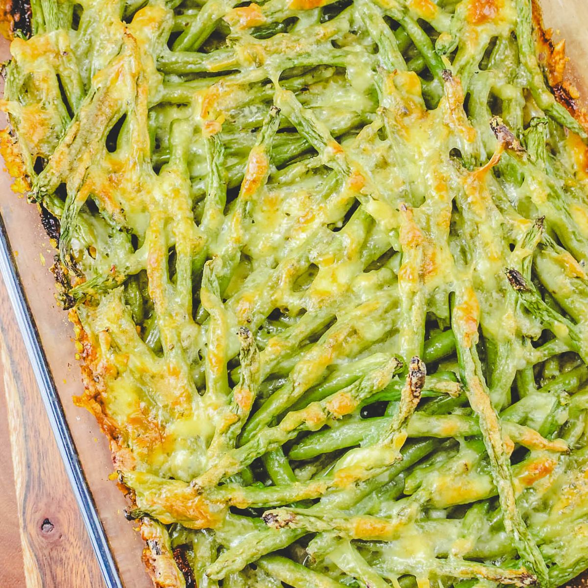 Green beans topped with a cheesy sauce in a glass casserole.
