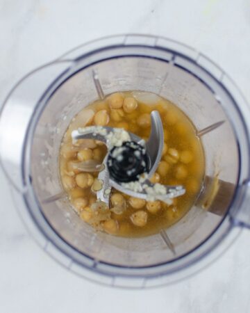 A food processor with chickpeas and onions to make hummus.