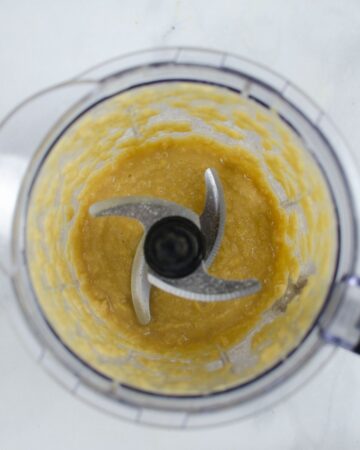 A food processor with pureed chickpeas and tahini to make homemade hummus.