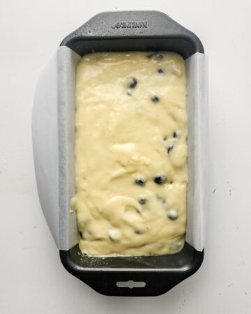 A loaf pan with batter to make a blueberry lemon loaf.