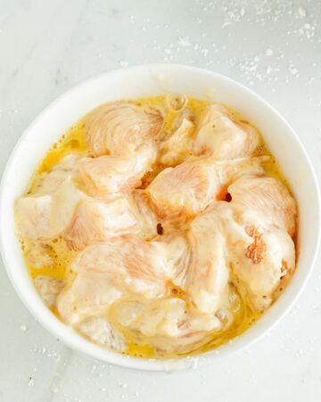 A white bowl with chicken pieces in an egg wash. 