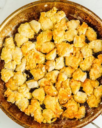 A saute pan with chicken pieces being browned to make orange chicken. 
