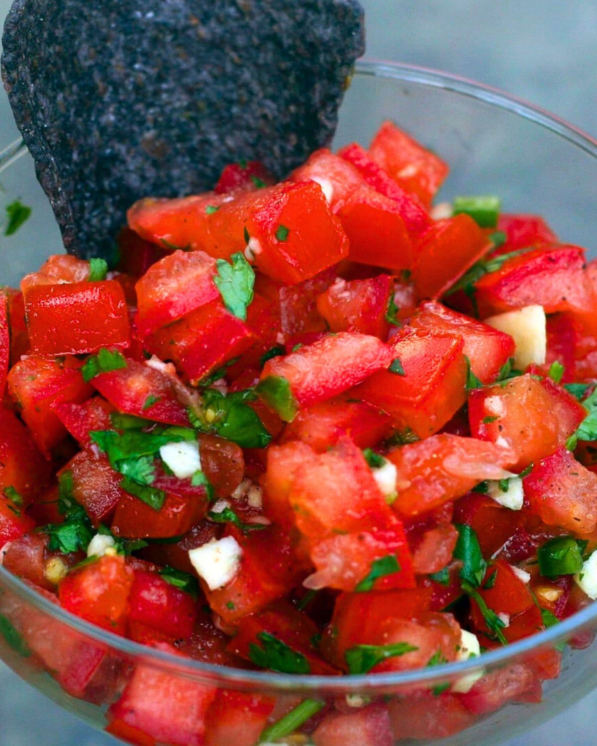 Authentic pico de gallo in a glass bowl with a blue tortilla chip.
