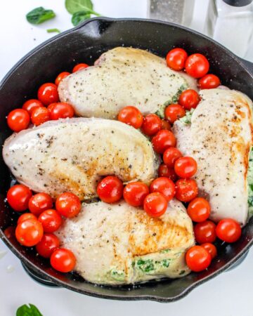 A cast iron pan with stuffed chicken breasts with tomatoes.