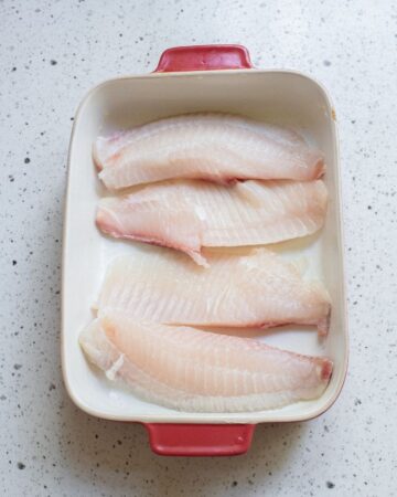 A baking dish with tilapia fillets in the pan.