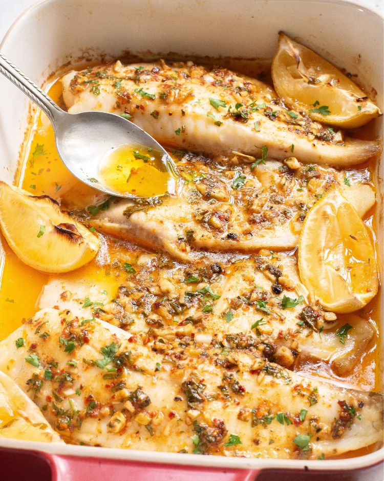 A baking dish with tilapia fillets in a lemon butter sauce with cajun spices.
