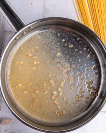 A saute pan with garlic and wine to make alfredo sauce