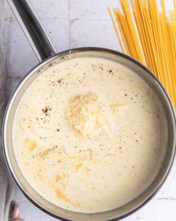 A saute pan with heavy cream, white wine, and garlic to make alfredo sauce.
