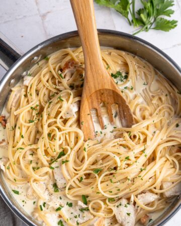 A large saute pan with pasta, alfredo sauce and diced chicken. 
