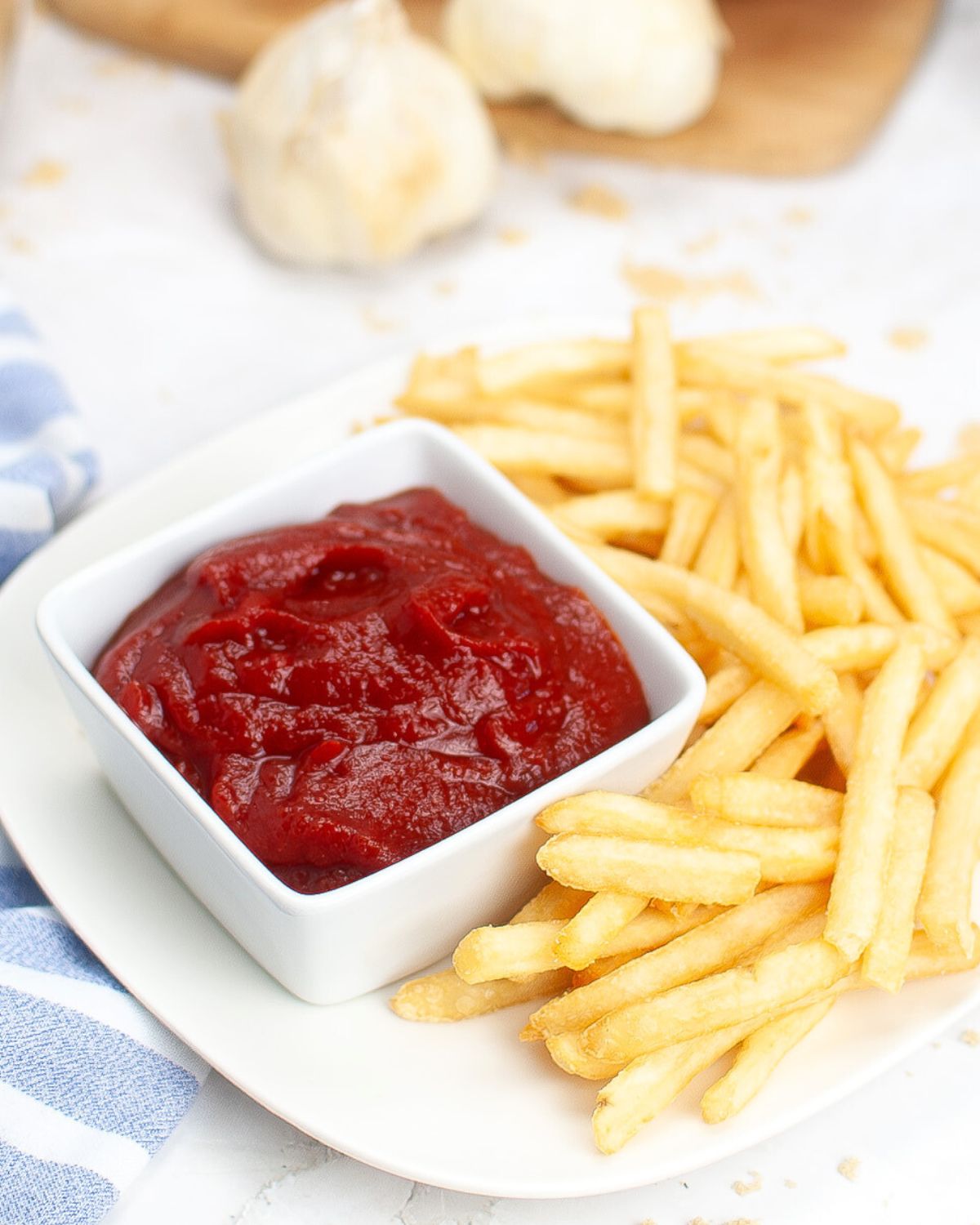 A white plate with french fries and a white bowl with homemade ketchup with tomato paste.