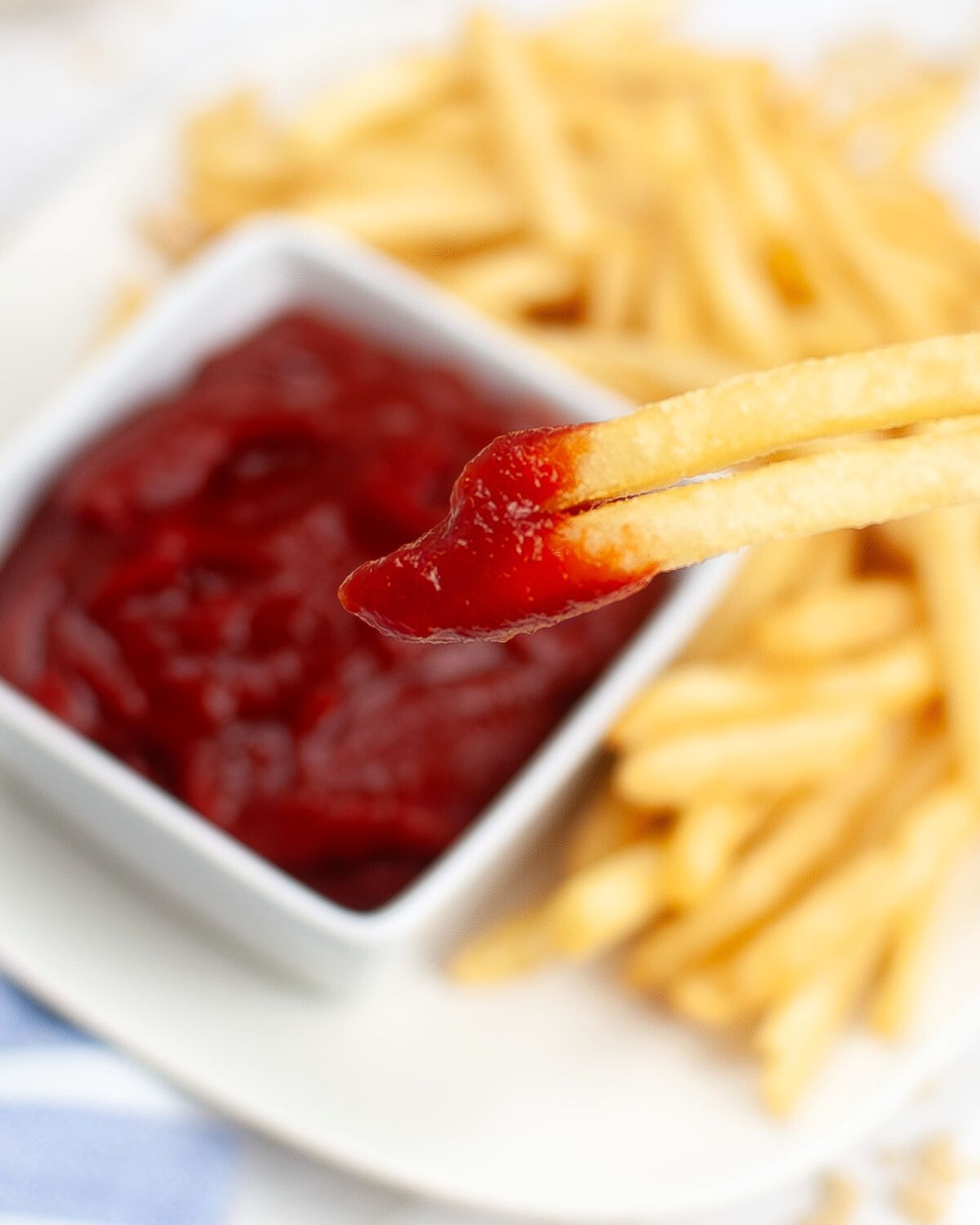 A white square bowl with homemade ketchup and french fries being dipped into the ketchup. 