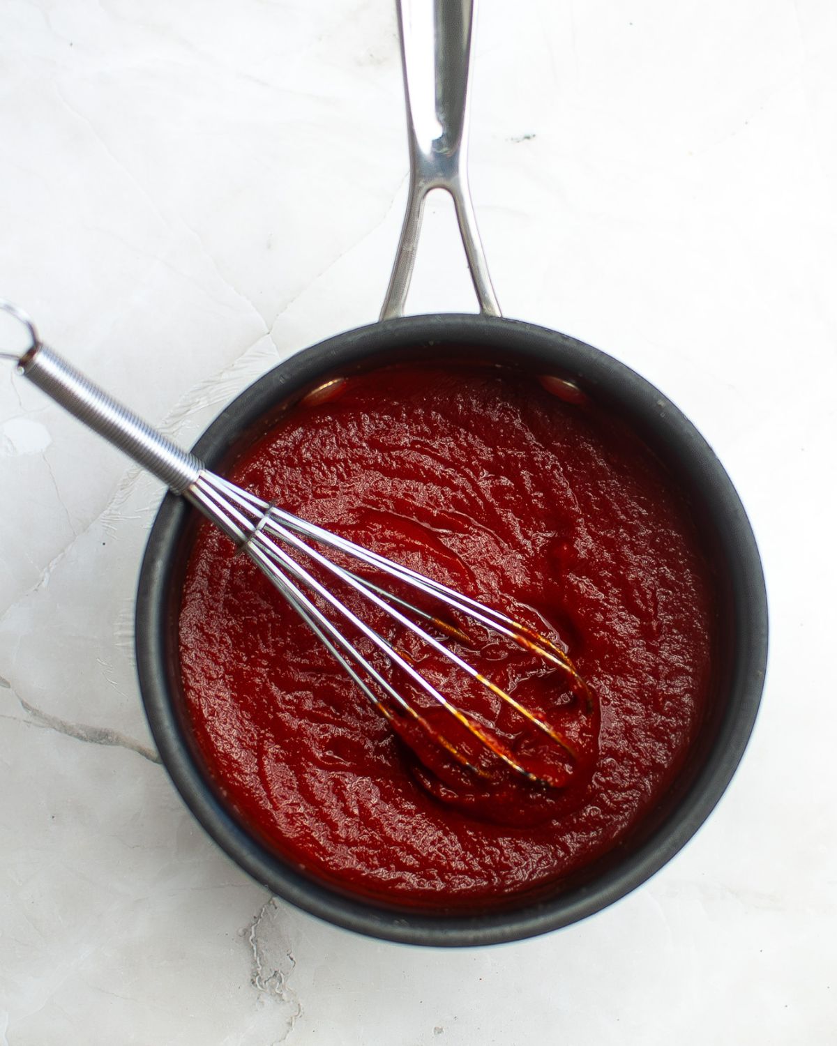 A large pot with homemade tomato ketchup with a whisk in the pot. 