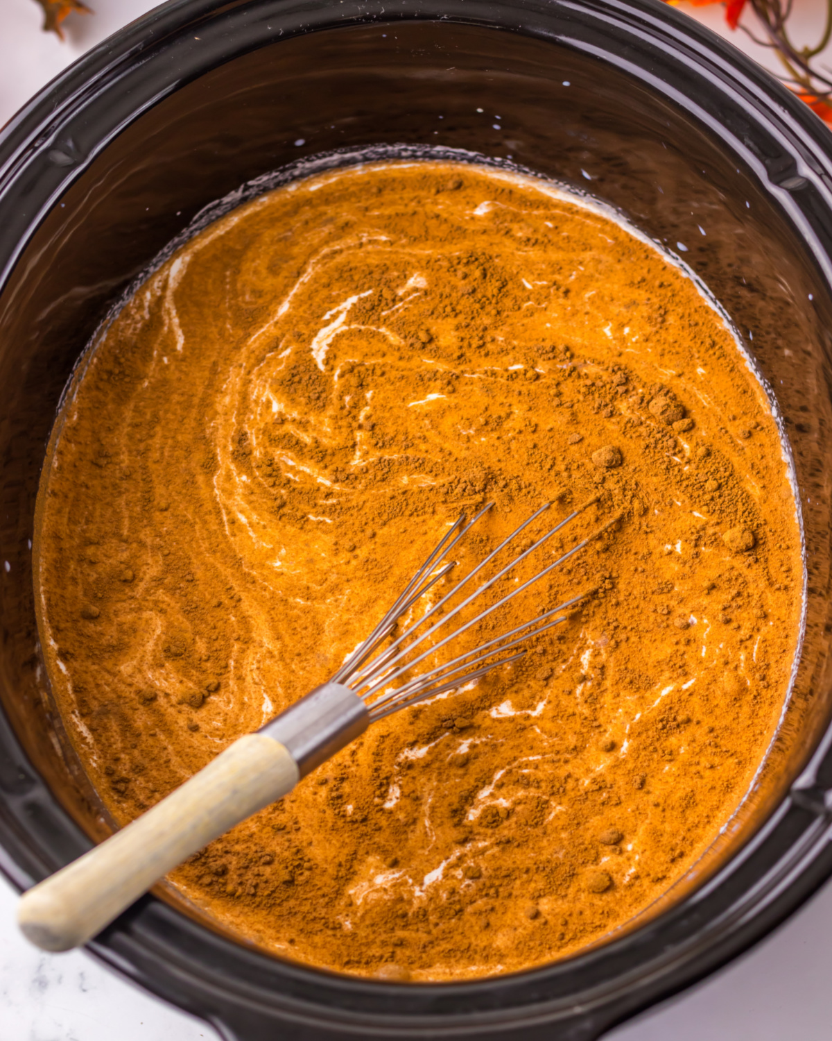 A slow cooker with pumpkin puree and spices with milk to make hot chocolate.