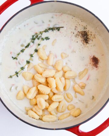 A large dutch oven with gnocchi, chicken, cream, and thyme to make a creamy chicken gnocchi soup. 