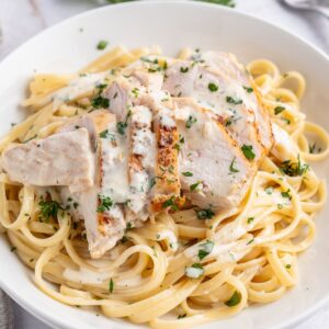A white plate with linguine and sliced chicken in alfredo sauce.