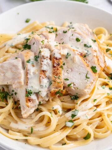 A white plate with linguine and sliced chicken in alfredo sauce.