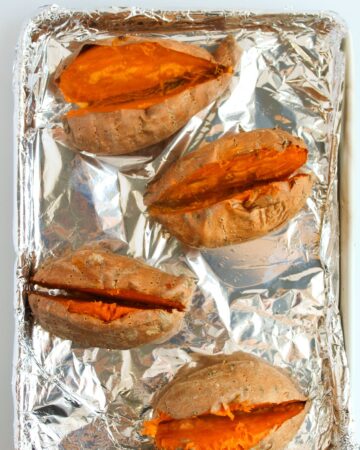 Sliced open baked sweet potatoes on a baking sheet. 
