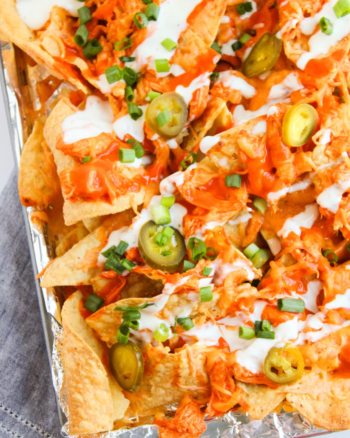 A baking tray with corn tortillas topped with buffalo chicken, cheddar cheese, ranch dressing, jalapenos, and green onions.
