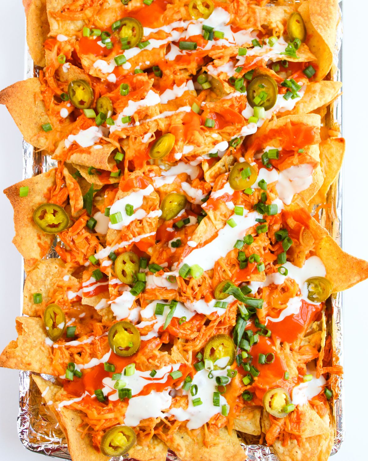 Baked buffalo chicken nachos topped with ranch dressing, pickled jalapenos and chopped green onions.