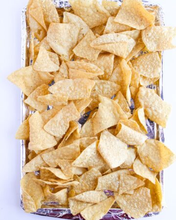 A baking tray with corn tortilla chips as the base of buffalo chicken nachos.