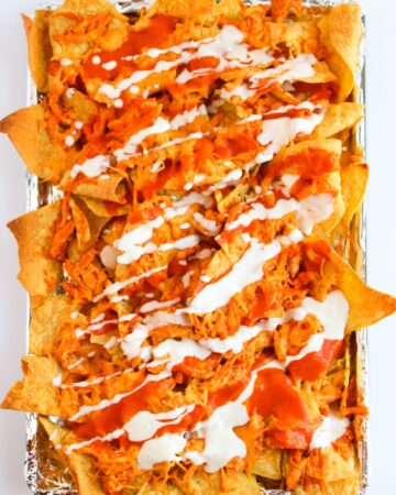 A tray of buffalo chicken nachos with ranch dressing.