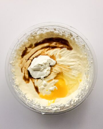 A glass bowl of cream cheese, sugar, eggs, and vanilla to make cinnamon roll cheesecake.