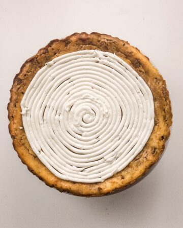 A cinnamon roll cheesecake being made with a top swirl layer of cream cheese frosting.