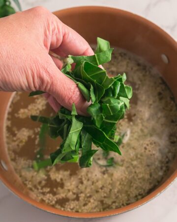 A ham hock, water, and collard greens in a large stock pot. 