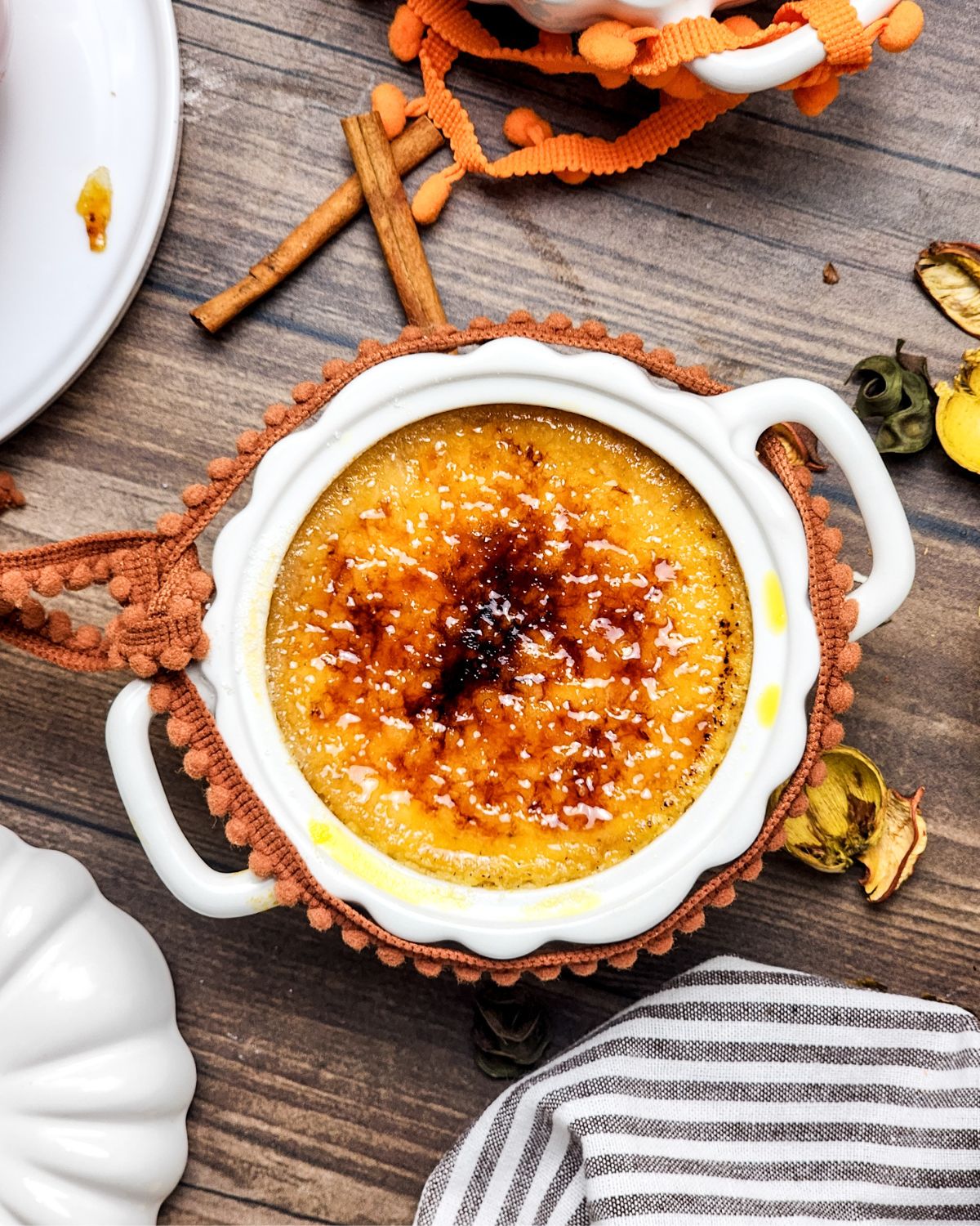 A white ramekin with pumpkin brulee in the bowl on a wooden plate.