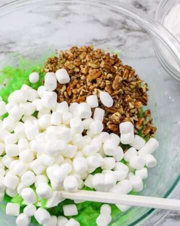 A glass bowl with pistachio pudding, marshmallows, and chopped pecans to make Watergate salad recipe.