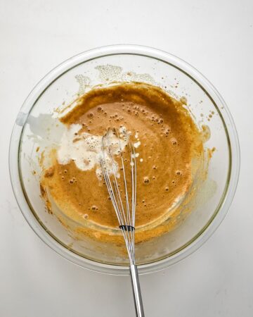 A glass bowl with eggs, heavy cream, and pumpkin spice.