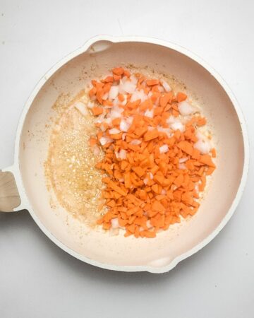 A skillet with carrots and onion to make a skillet chicken pot pie with biscuits.